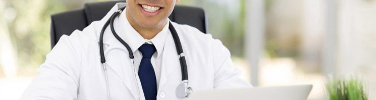 Médico sorrindo sentado digitando no computador | O que é o e-Médico e como ele pode ser utilizado?
